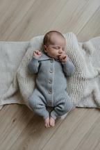 Baby in blue knit romper, hands by face
