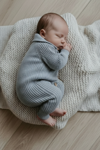 Baby in blue knit romper, side curl pose